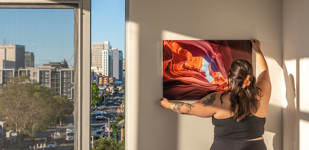 Woman hanging vibrant aluminum photo print of Antelope Canyon during golden hour — custom metal wall art by Aluminyze showcasing premium aluminum photo printing for home decor.